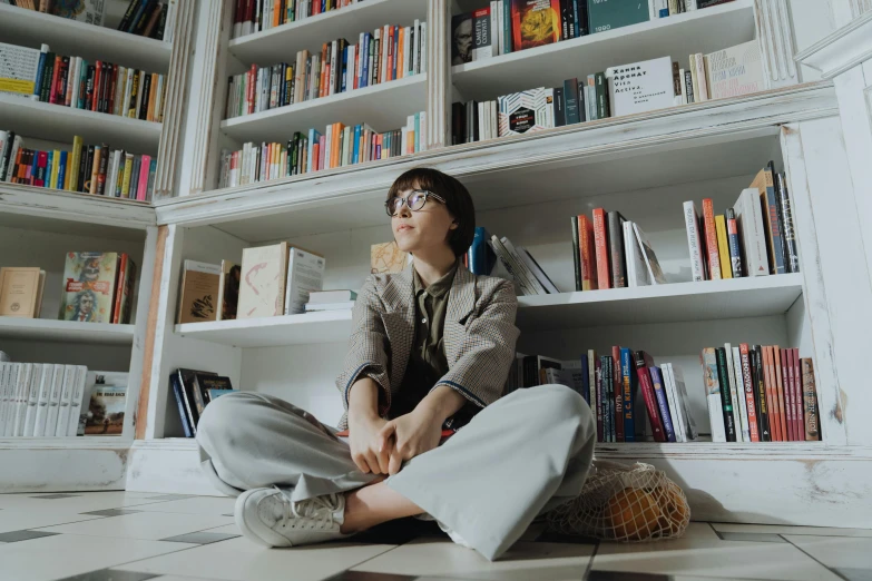 a woman sitting on the floor in front of a bookshelf, by Nina Hamnett, pexels contest winner, portrait androgynous girl, girl wearing round glasses, jung jaehyun, sitting on a store shelf