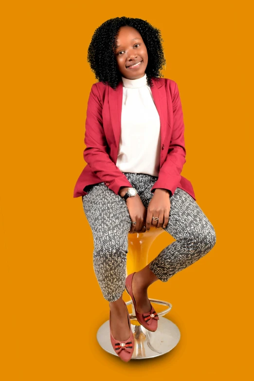 a woman sitting on top of a yellow chair, by Ingrida Kadaka, pexels, red sweater and gray pants, wearing a blazer, with afro, orange tones