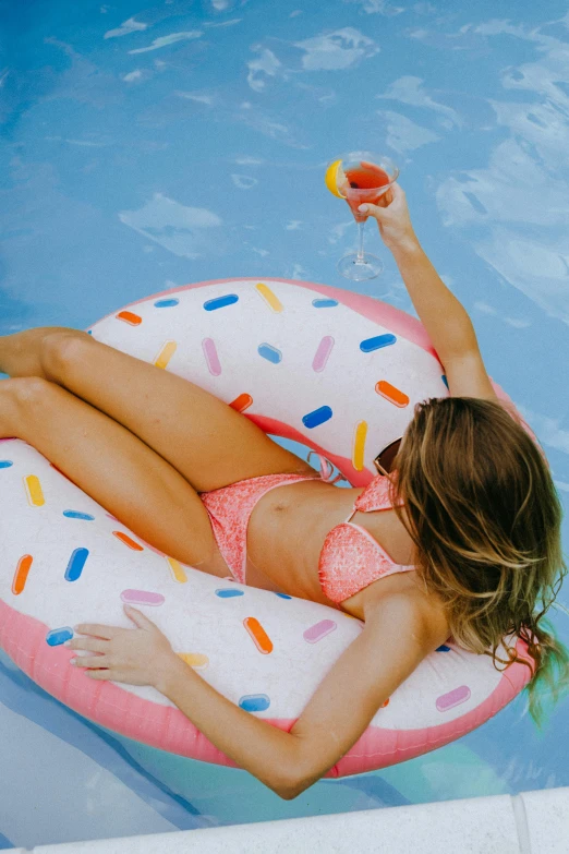 a woman laying on an inflatable donut in a pool, unsplash contest winner, pop art, holding a drink, floating pieces, pink frosted donut, sydney sweeney