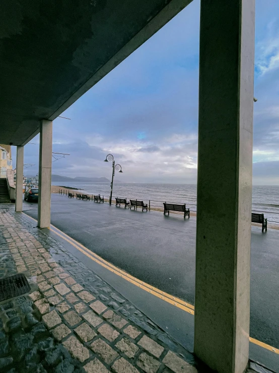 a couple of benches sitting on the side of a road, inspired by Thomas Struth, unsplash, seaside victorian building, panoramic view, wet street, profile image