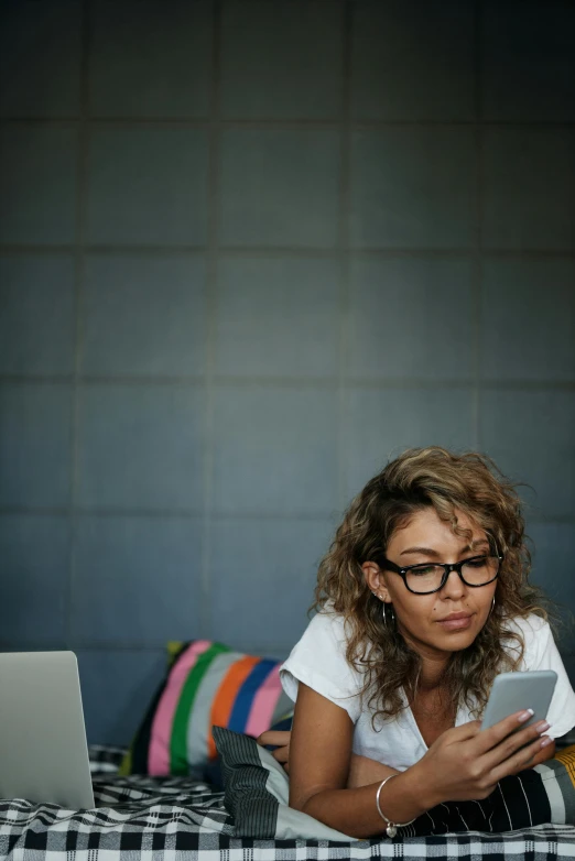 a woman laying on a bed using a cell phone, trending on pexels, sitting in office, with glasses on, curly haired, looking serious