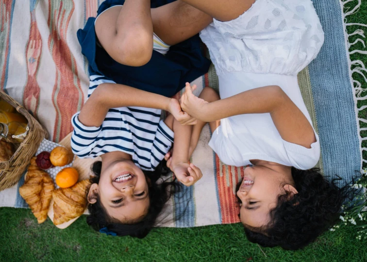 a couple of people laying on top of a blanket, by Carey Morris, pexels contest winner, happy kid, picnic, sisters, hispanic