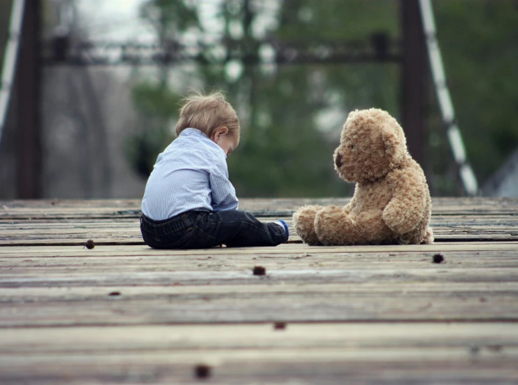 a small child sitting on a wooden floor next to a teddy bear, by Jesper Knudsen, pexels contest winner, on a bridge, friends, boys, covered in