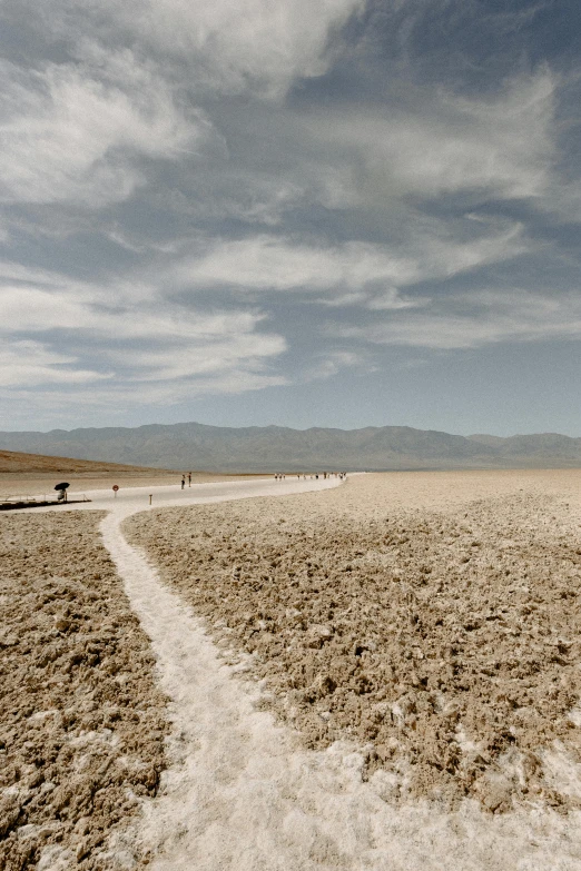 a man flying a kite on top of a sandy beach, by Kristin Nelson, unsplash contest winner, land art, icy road on a planet of lava, death valley, people walking around, ai weiwei and gregory crewdson