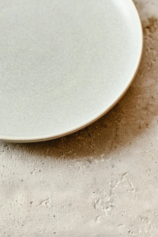 a white plate sitting on top of a table, inspired by Maruyama Ōkyo, trending on unsplash, process art, sand color, close up angle, light grey, granular detail