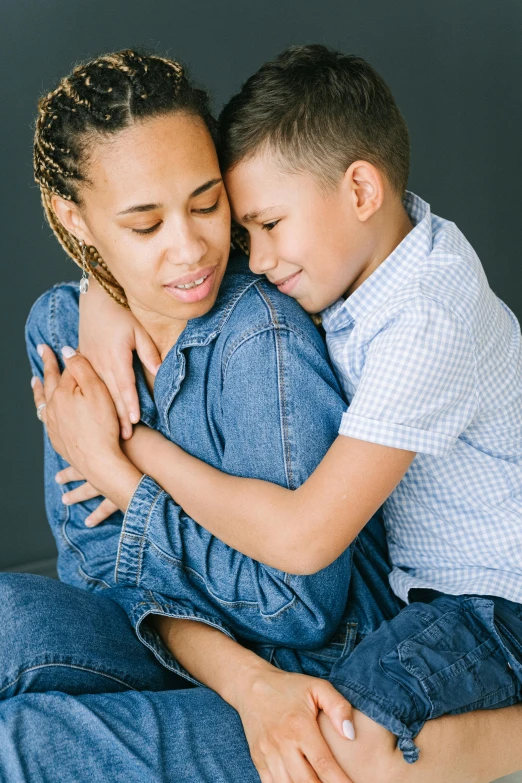 a woman sitting next to a boy on top of a bed, hugging her knees, in front of a black background, compassionate, slide show