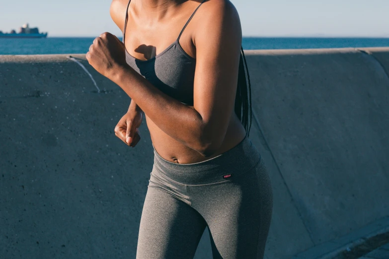 a woman running by the ocean on a sunny day, trending on pexels, happening, belly button showing, in gunmetal grey, detail shot, hunched shoulders