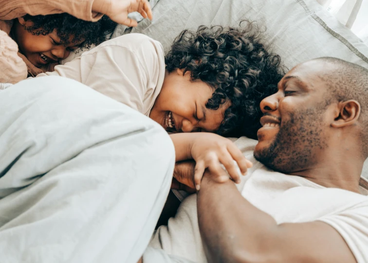 a man and woman laying in bed next to each other, pexels contest winner, father with child, smiling playfully, black man, piled around