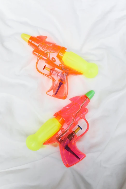 a couple of water guns laying on top of a bed, multi - coloured