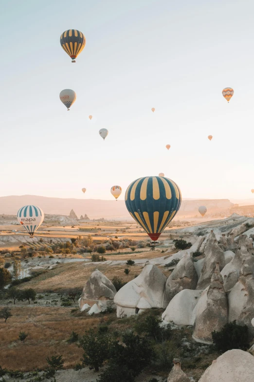 a group of hot air balloons flying over a rocky landscape, pexels contest winner, trending on vsco, turkey, rolling hills, distant photo