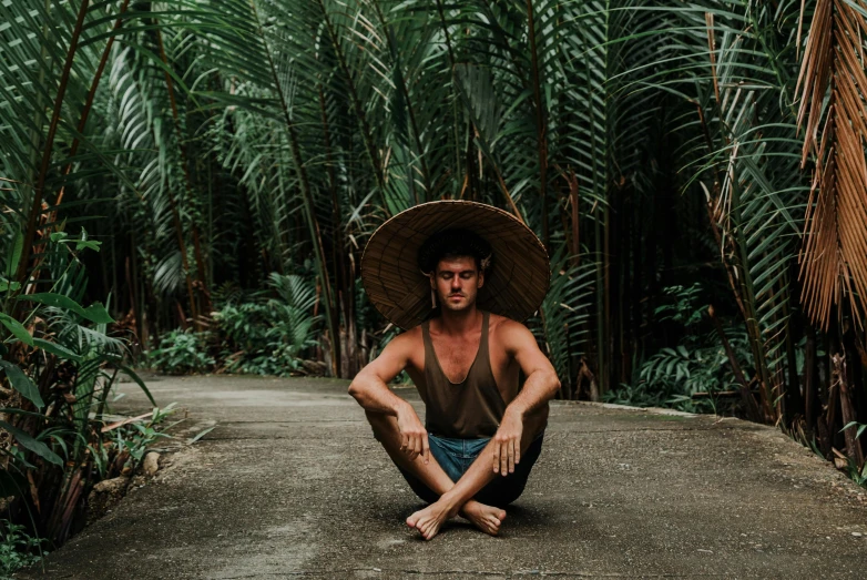 a man sitting on the ground with a hat on, by Daniel Lieske, sumatraism, lush paradise, squatting pose, avatar image