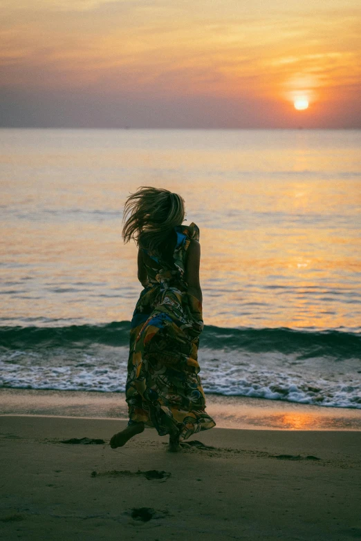 a woman walking on a beach at sunset, pexels contest winner, renaissance, sundress, half turned around, vibrant patterns, windy