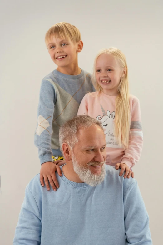 a man sitting in front of a laptop with two children on his shoulders, a picture, inspired by Doug Ohlson, grey trimmed beard, pastel clothing, wearing a sweater, model shoot