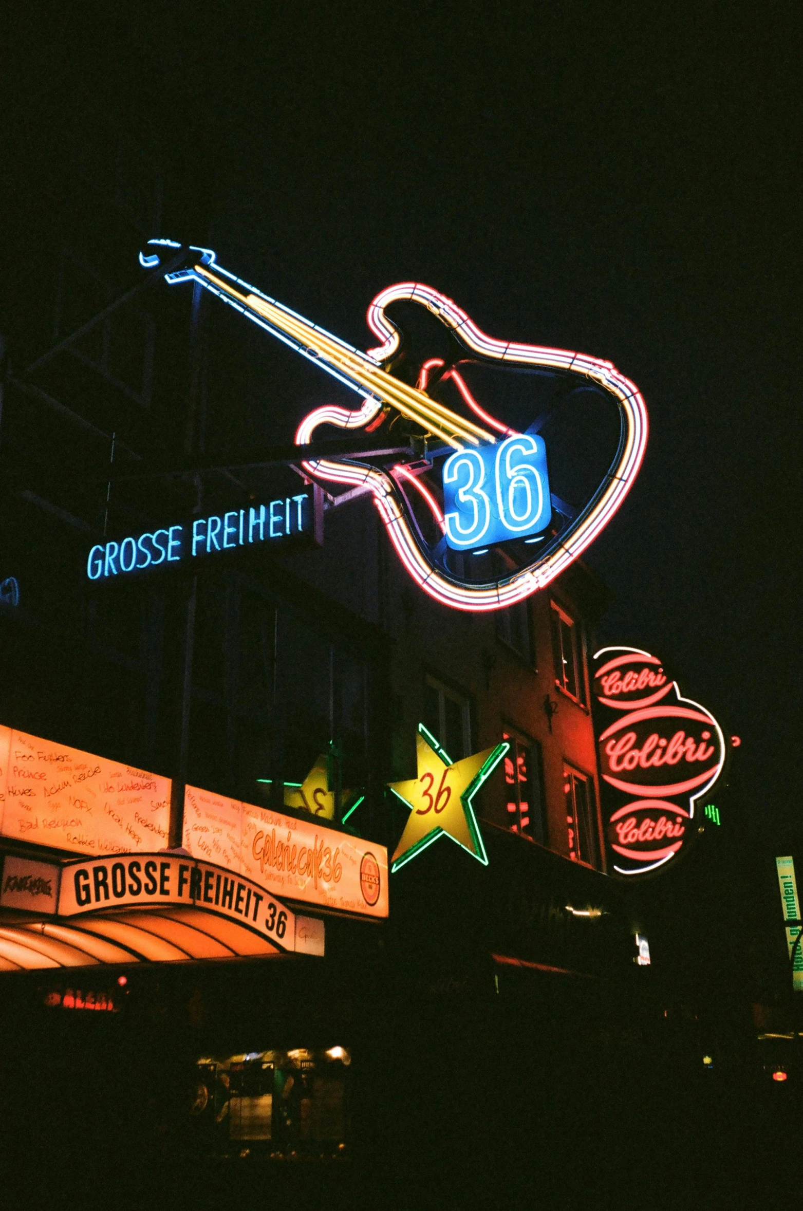 a group of neon signs on the side of a building, an album cover, by Karl Gerstner, pexels, 1950s photograph, concert, summer night, a 35mm photo