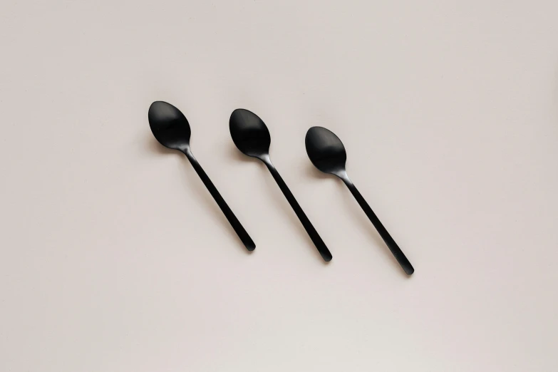 three spoons sitting next to each other on a table, an album cover, by Emma Andijewska, minimalism, all black matte product, spatula, enamel, three quarter angle