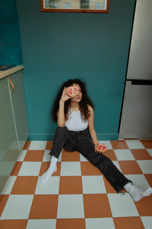 a woman sitting on a checkered floor holding a slice of pizza, by Nathalie Rattner, trending on pexels, long wild black curly hair, lemonade, ashteroth, standing in corner of room