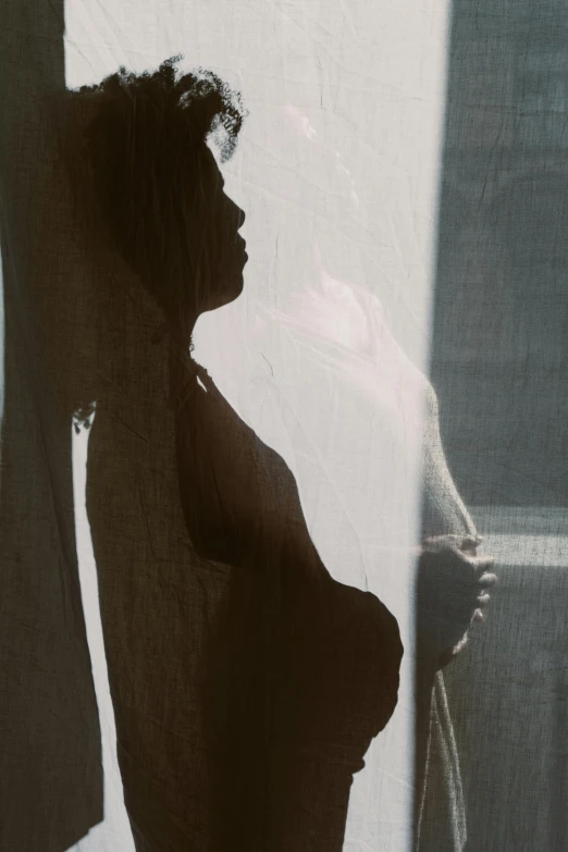 a pregnant woman standing in front of a window, by Elsa Bleda, pexels contest winner, conceptual art, sun and shadow, black young woman, side view close up of a gaunt, instagram post