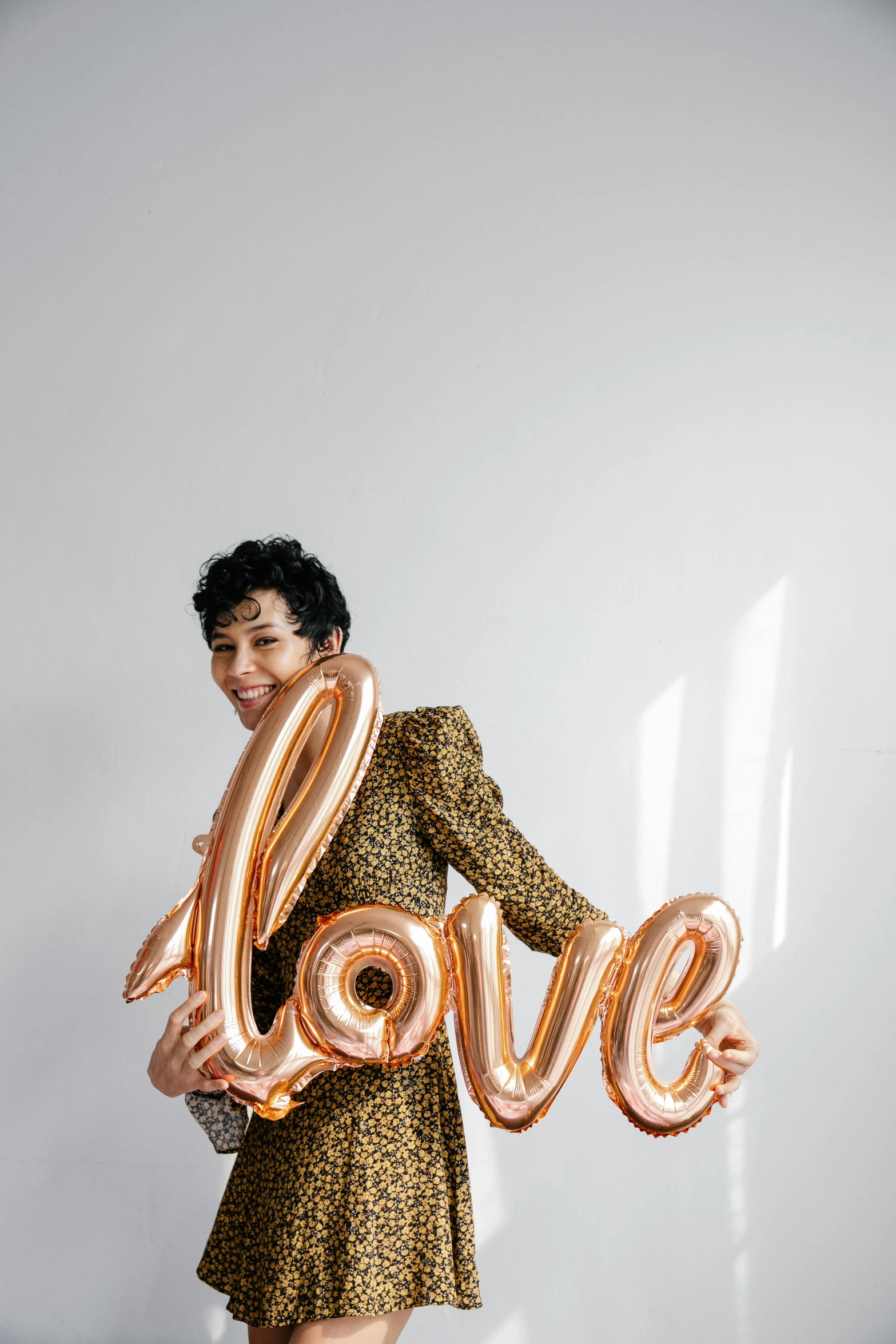 a woman holding a balloon shaped like the word love, an album cover, trending on pexels, studio portrait, party balloons, androgynous person, rebecca sugar