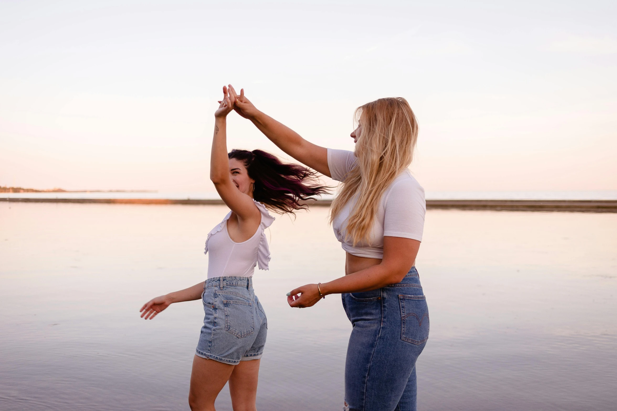 a couple of women standing on top of a beach, unsplash, happening, dancing with each other, hair fanned around, charli bowater and artgeem, standing next to water