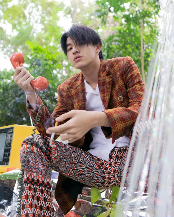 a man sitting in front of a fountain holding tomatoes, an album cover, inspired by Xia Yong, stripey pants, wearing a flannel shirt, wearing a colorful men's suit, in style of thawan duchanee