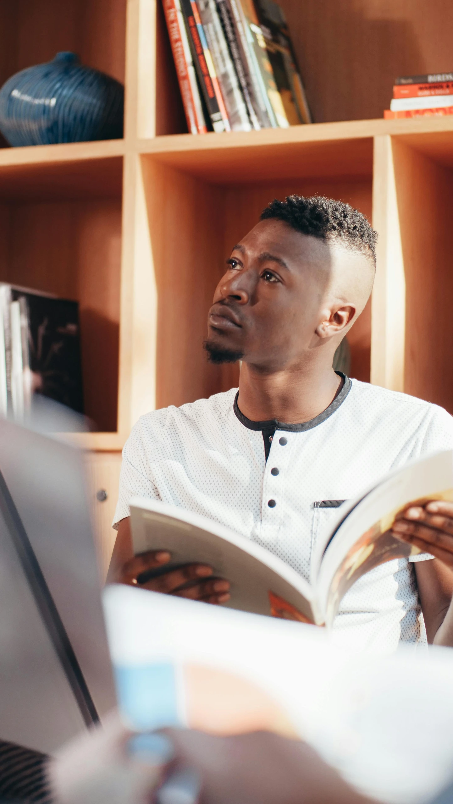 a man sitting on a couch reading a book, inspired by Barthélemy Menn, pexels contest winner, man is with black skin, library background, julian ope, studious