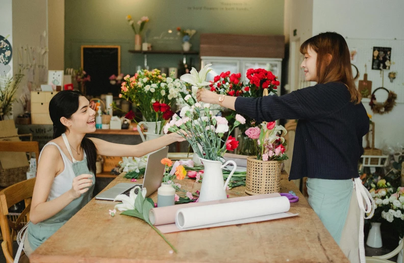 two women sitting at a table in a flower shop, pexels contest winner, reaching out to each other, slightly minimal, diy, thumbnail