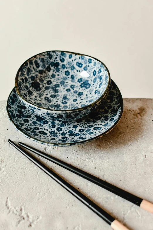 a bowl and two chopsticks sitting on a table, inspired by Yamaguchi Kayo, unsplash, mingei, blue - petals, made of glazed, spots, petite