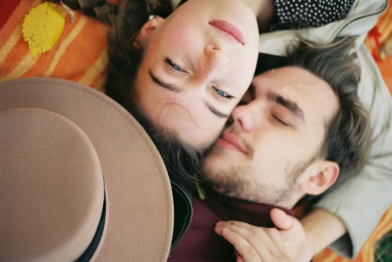 a man and a woman laying on a blanket, by Anita Malfatti, trending on pexels, hat covering eyes, looking up at camera, making out, close up face