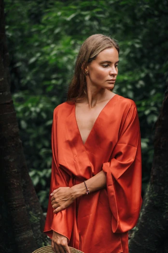 a woman in an orange dress holding a basket, by Emma Andijewska, trending on unsplash, wearing a luxurious silk robe, jungle gown, dark red, looking to the side