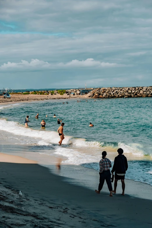 a group of people standing on top of a beach next to the ocean, swimming in ocean, reykjavik, near a jetty, cannes