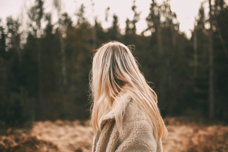 a woman standing in a field with trees in the background, trending on pexels, blond fur, cozy aesthetic, half turned around, girls