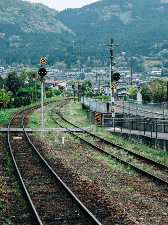 a train traveling down train tracks next to a lush green hillside, an album cover, unsplash, japanese rural town, voge photo, 🚿🗝📝, electrical signals
