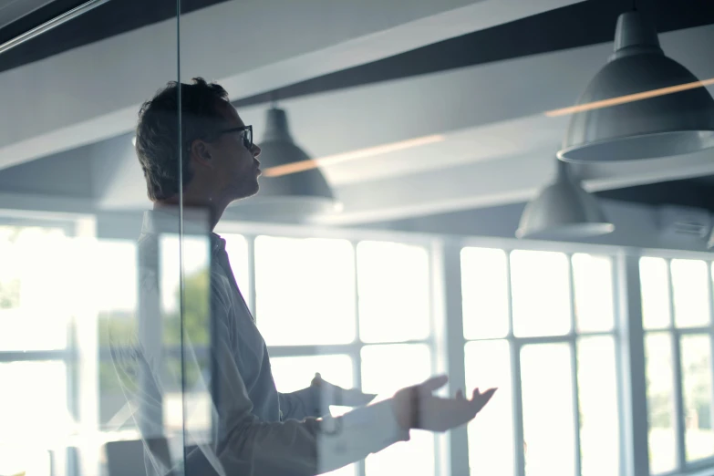 a man standing in front of a glass wall, talking, in a meeting room, hovering indecision, best practice