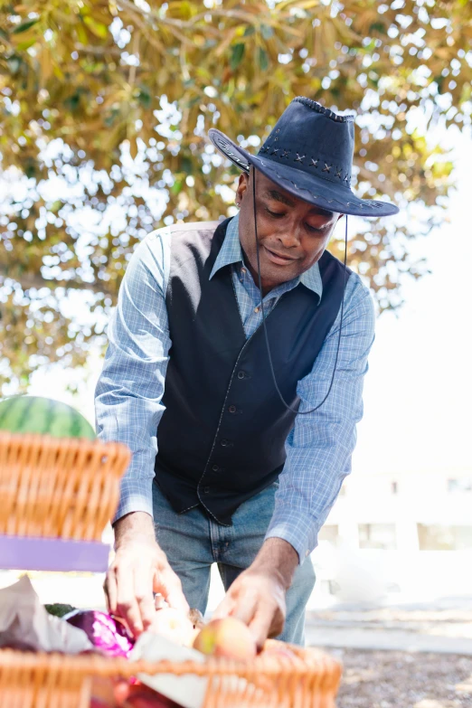 a man in a hat picking apples from a basket, lance reddick, cowboy themed, wearing a purple cap, ground breaking