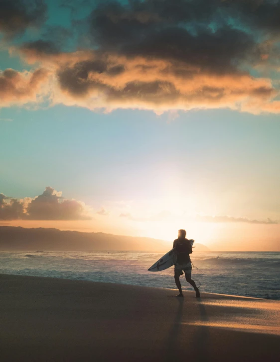 a person walking on a beach with a surfboard, during a sunset