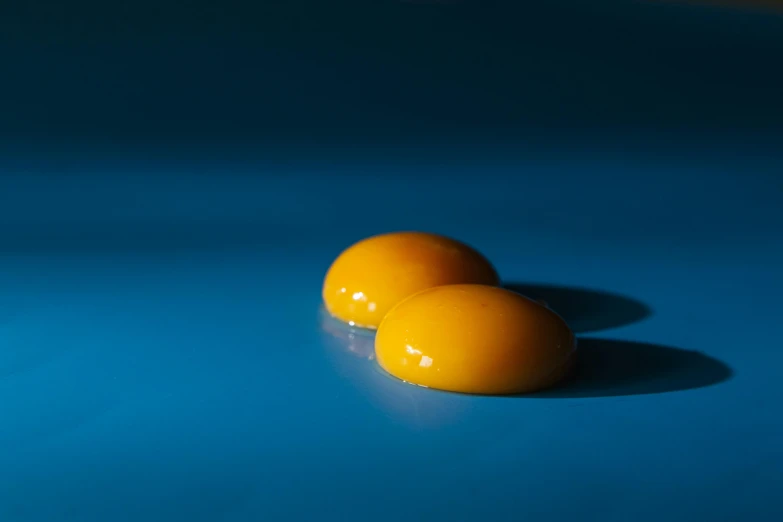 two eggs sitting next to each other on a blue surface, by Jan Rustem, plasticien, gradient yellow, shot on sony a 7 iii, pills, farming