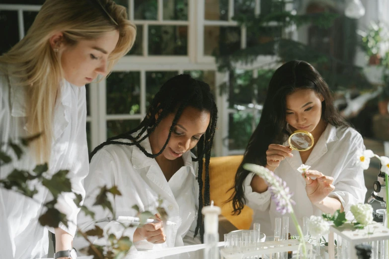 a group of women standing next to each other in a lab, by Emma Andijewska, pexels contest winner, gardening, white and gold robes, test tubes, looking across the shoulder