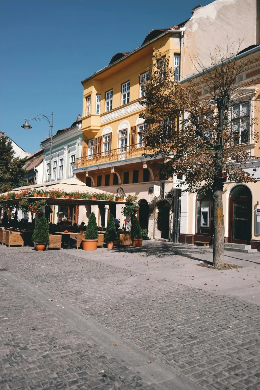 a cobblestone street with tables and umbrellas, inspired by Jenő Barcsay, art nouveau, yellow awning, palace, slovakia, shot onfilm