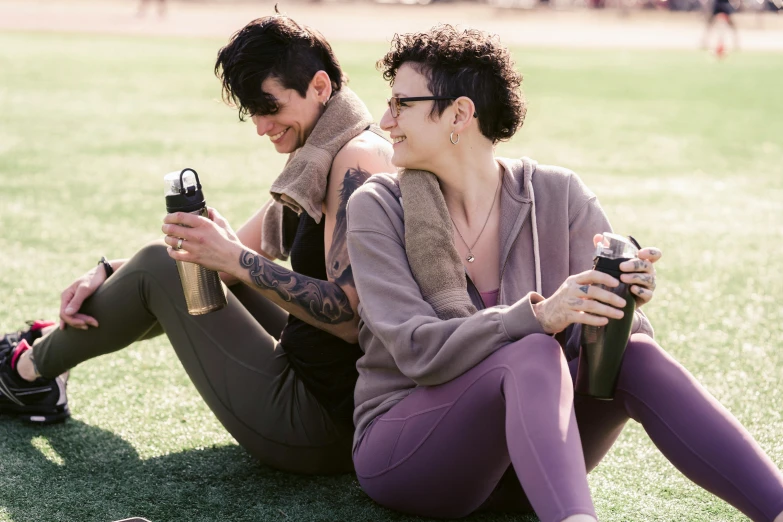 a man and a woman sitting on the grass, trending on pexels, water bottles, lesbian, wearing a purple sweatsuit, brunettes