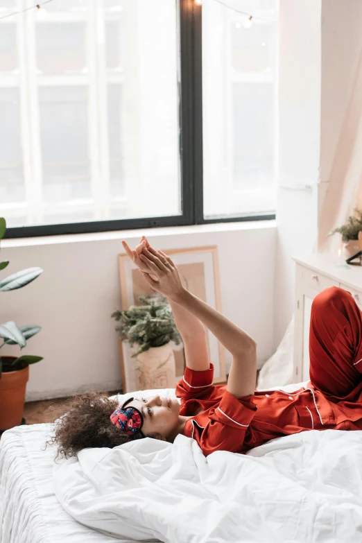 a woman laying on top of a bed wearing headphones, a cartoon, trending on pexels, hands in air, wearing red clothes, location in a apartment, in a white boho style studio