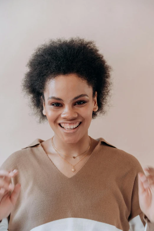 a woman that is standing up with her hands in the air, dark short curly hair smiling, big forehead, plain background, portrait featured on unsplash