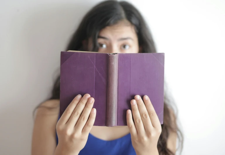 a woman holding a purple book in front of her face, pexels contest winner, surprised, indian girl with brown skin, wearing purple undershirt, gif