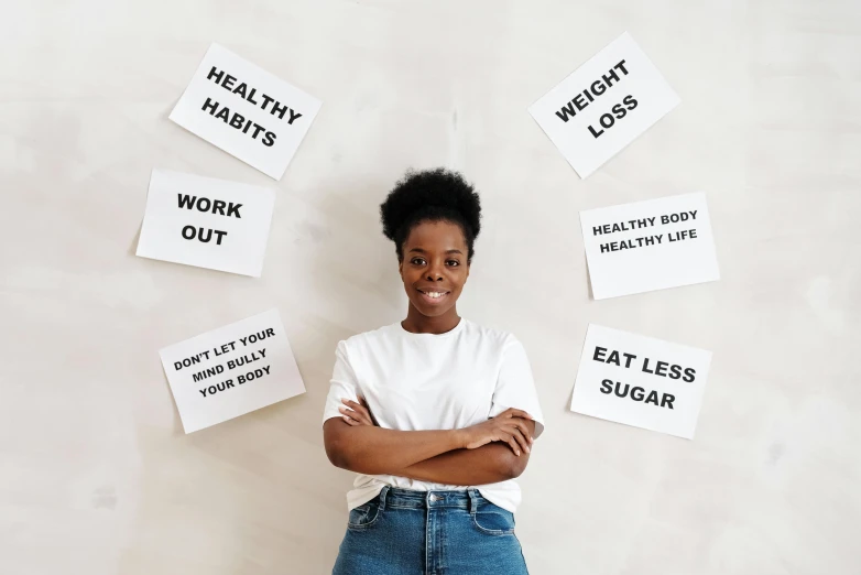 a woman standing in front of a wall with signs on it, pexels contest winner, healthy, on a white table, black young woman, background image