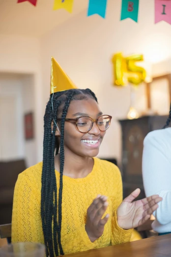 two women sitting at a table in front of a cake, pexels contest winner, happening, black teenage girl, wearing a party hat, silver and yellow color scheme, pictured from the shoulders up