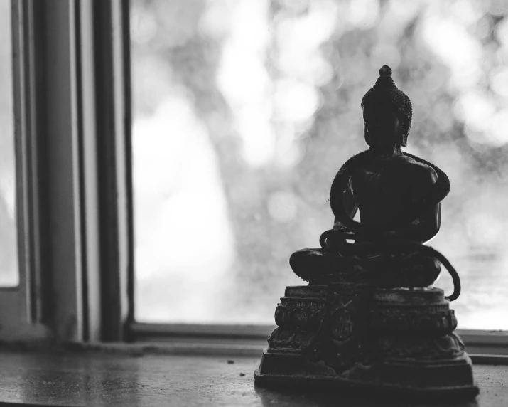 a black and white photo of a buddha statue, a statue, unsplash, minimalism, next to window, karma sutra, sittin