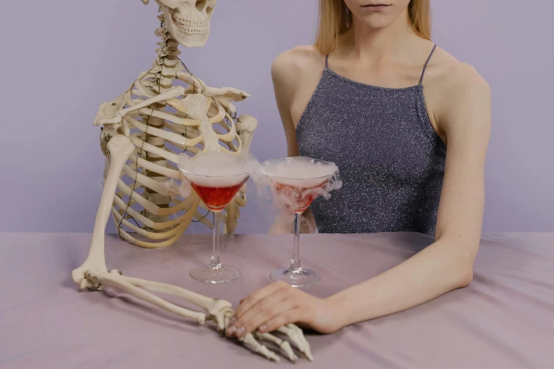 a woman sitting at a table with a skeleton behind her, inspired by Elsa Bleda, trending on pexels, wearing a cocktail dress, purple drank, mary jane ansell, vests and corsets