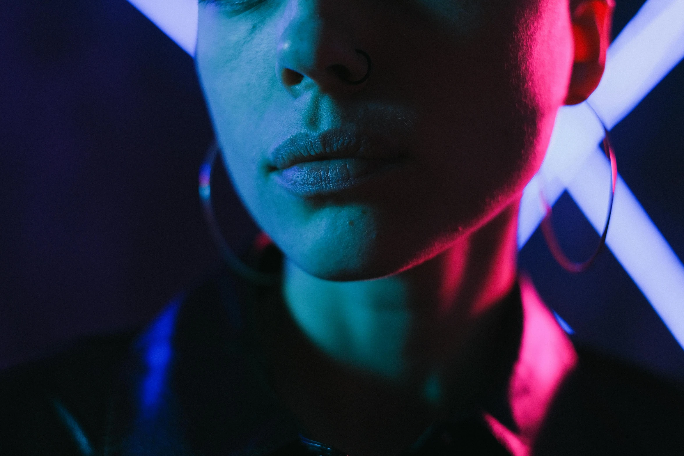 a woman standing in front of a neon light, inspired by Elsa Bleda, trending on pexels, synchromism, androgynous face, neck zoomed in from lips down, reflecting light in a nightclub, septum piercing