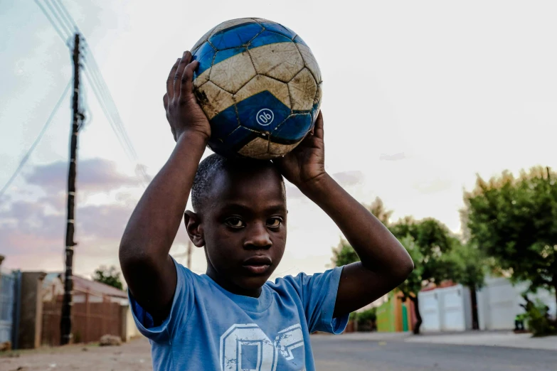 a young boy holding a soccer ball on his head, by Daniel Lieske, pexels contest winner, happening, township, instagram post, rosen zulu, by greg rutkowski