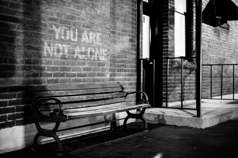 a black and white photo of a bench in front of a building, by Lizzy Ansingh, pexels, street art, message, painted on a brick wall, it's you and me, hes alone