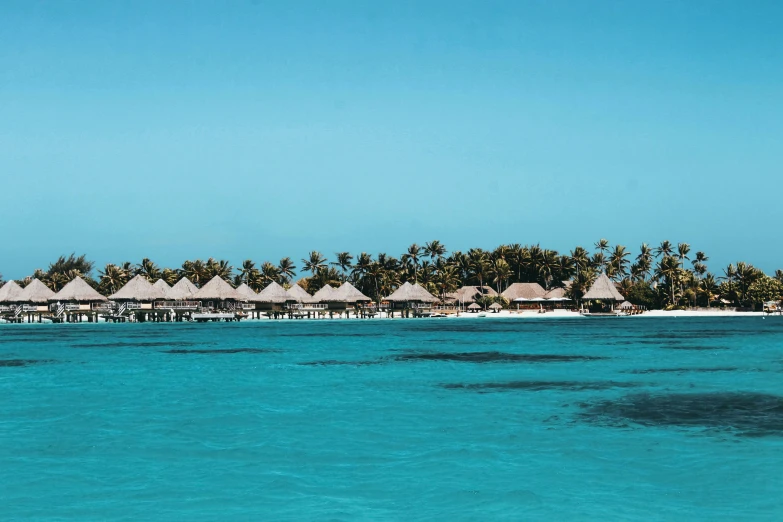 a large body of water surrounded by palm trees, a colorized photo, pexels contest winner, hurufiyya, thatched roofs, turquoise ocean, huts, brochure